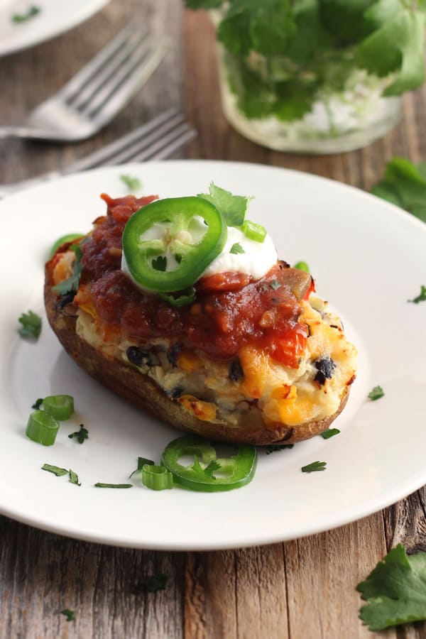 A white plate with a twice baked potato topped with salsa and a slice of jalapeno.