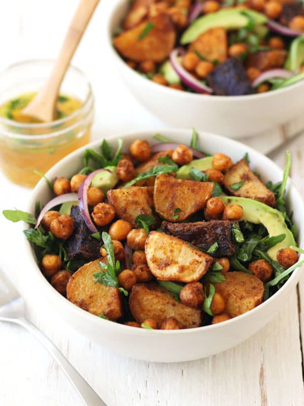 A white table with two bowls full of salad with a mason jar of dressing.