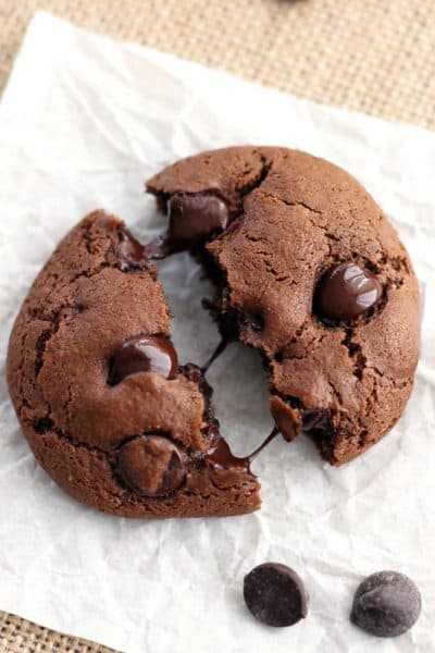 A chocolate cookie broken in half on a piece of parchment paper.