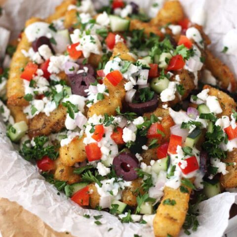 Close up of crispy fries covered with feta, tomatoes, and fresh parsley.