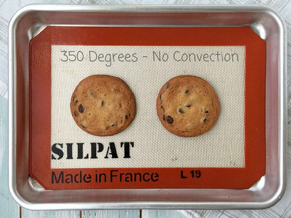 Two baked chocolate chip cookies on a pan.