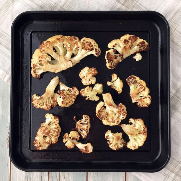 Roasted cauliflower on a black toaster oven baking pan