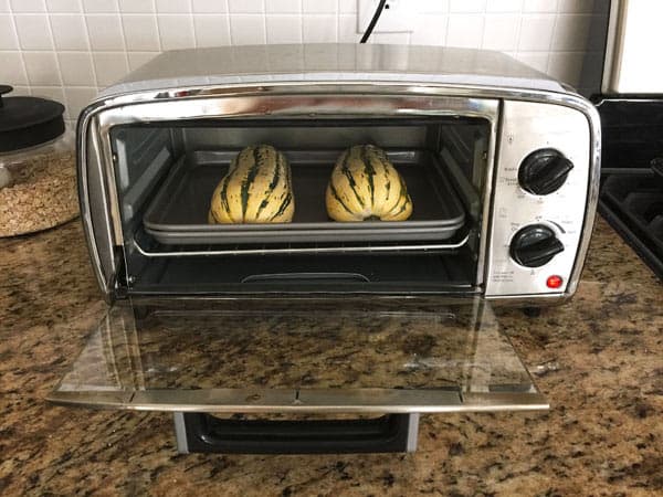 Two halves of delicata squash cooking in a small toaster oven.