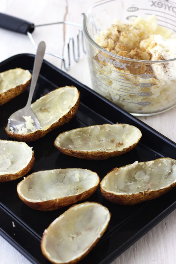 A baking sheet with baked potato halves scooped out with a spoon.
