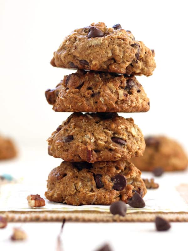 A stack of four chocolate chips cookies surrounded by nuts and chocolate chips.