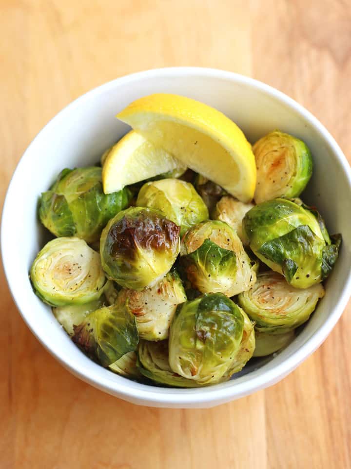 Roasted Brussels sprouts in a bowl with lemon wedges.