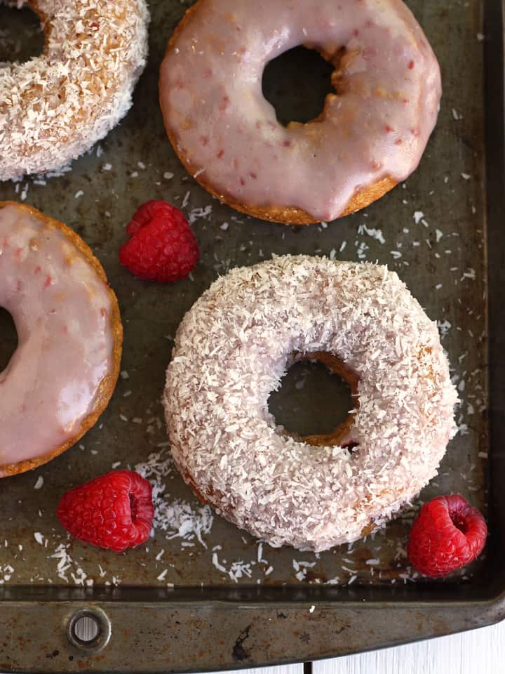 Baked donuts and fresh raspberries on a metal baking sheet.