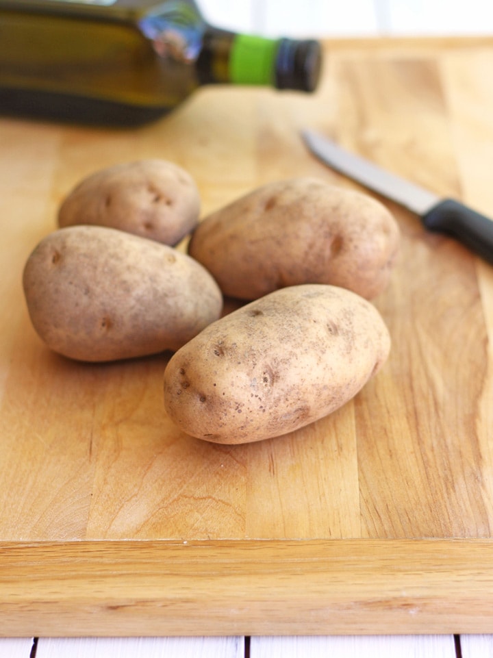 Raw russet potatoes on a cutting board.