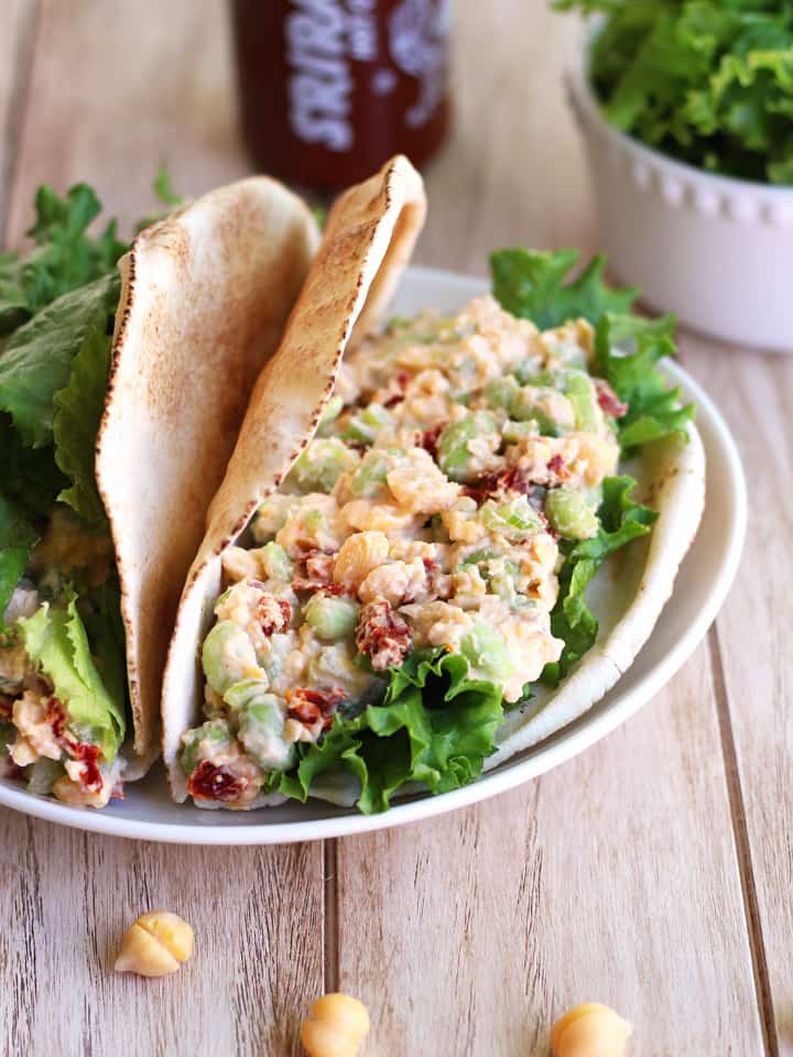 Spicy Chickpea Edamame Salad Pitas Pita sandwiches on a white plate next to a bottle of sriracha.