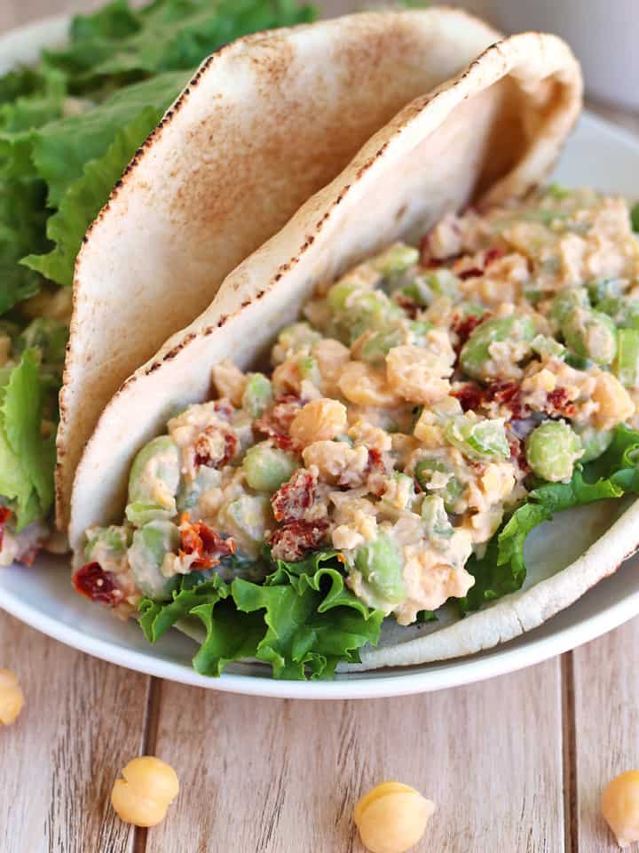 Spicy Chickpea Edamame Salad Pitas Filled pitas on a white plate on a wooden table with loose chickpeas.