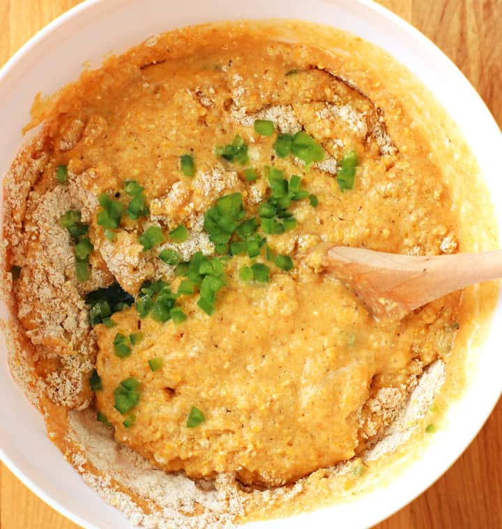 A white bowl with cornbread batter stirred with a wooden spoon.