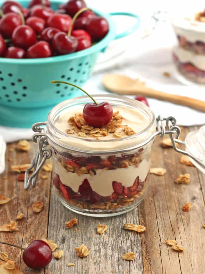 A small mason jar layered with yogurt, granola, and fresh cherries.
