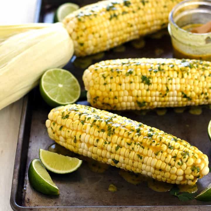 Sheet pan of baked corn with lime wedges and butter.
