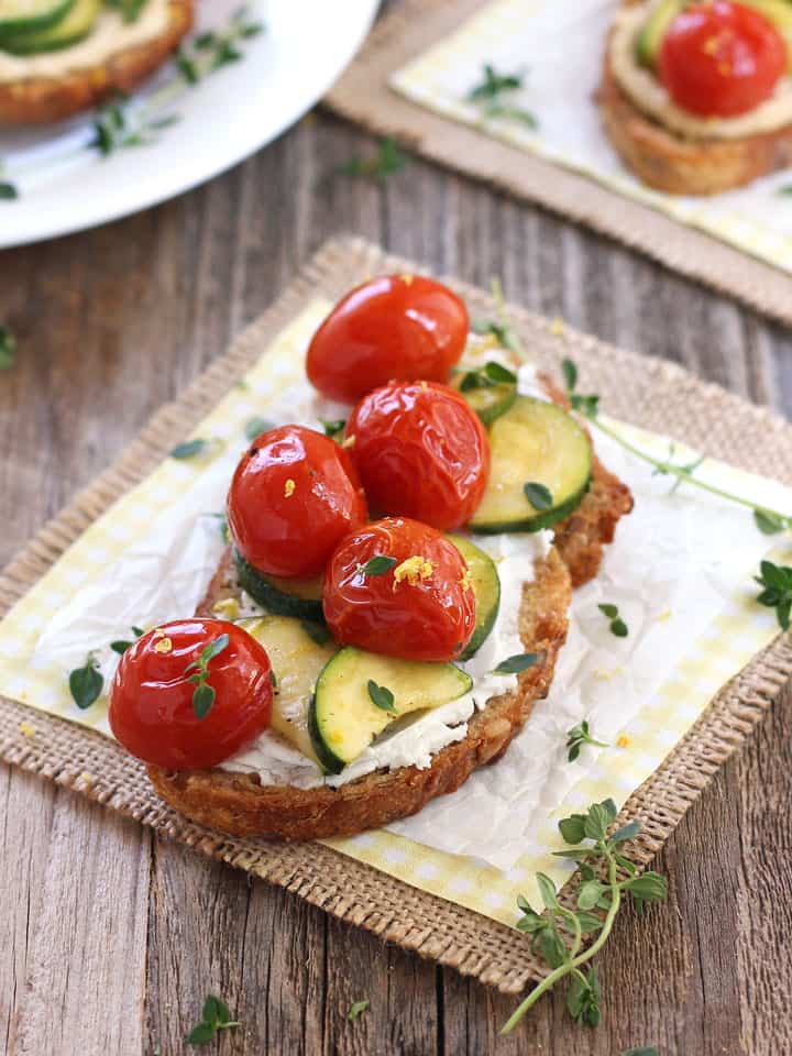 Veggie crostini on a wooden table with a sprig of fresh thyme.