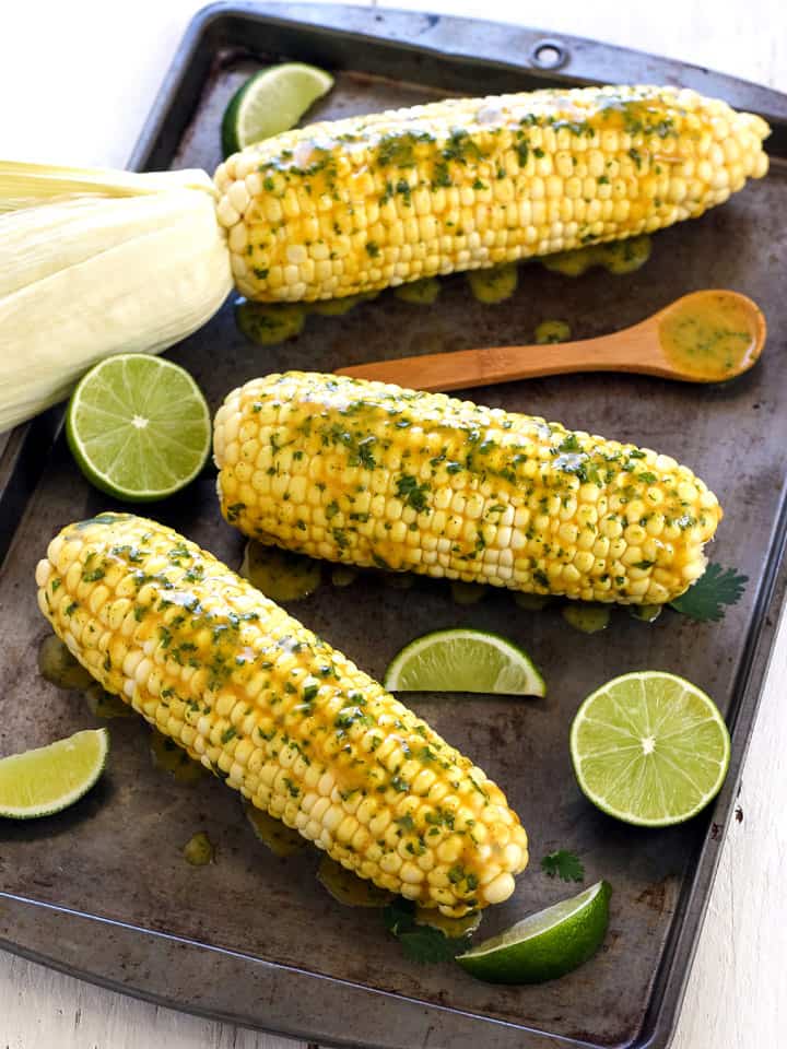Baked corn cobs on a dark sheet pan topped with coconut butter.