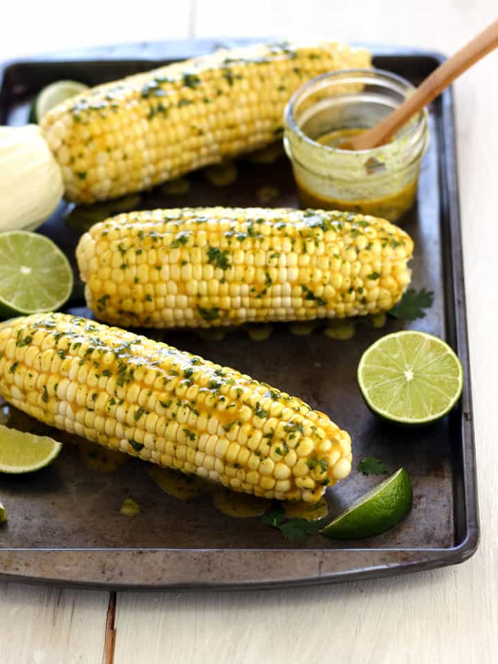Sheet pan of baked corn with lime wedges and butter.