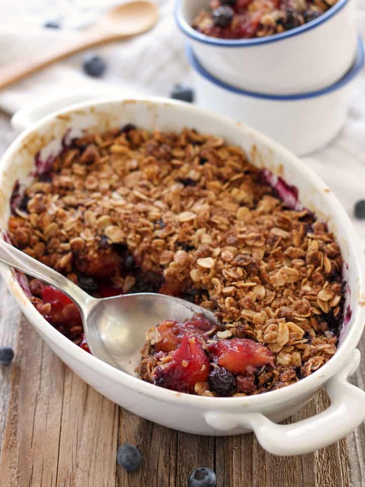 A large spoon scooping fruit crisp out of a baking dish.