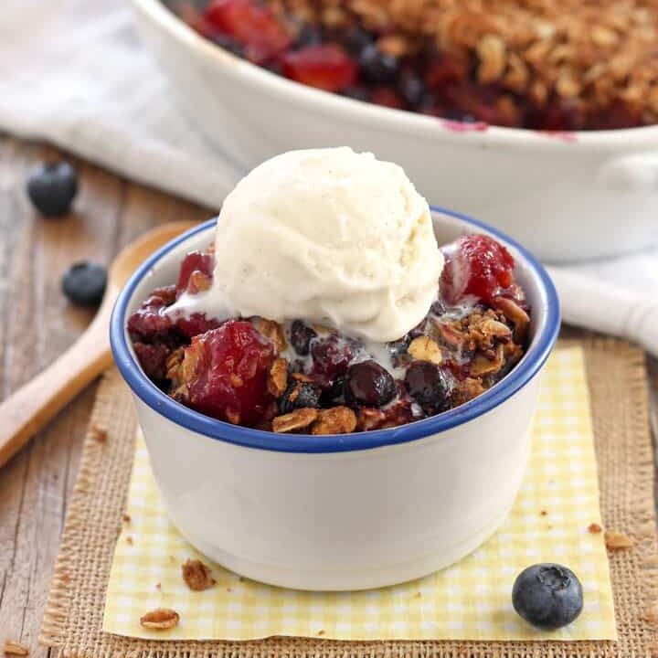 Small bowl of fruit crisp topped with a scoop of vanilla ice cream.