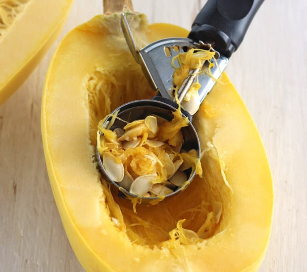 Ice cream scoop scooping seeds out of a raw spaghetti squash.