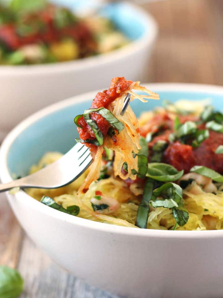 Fork scooping spaghetti squash out of a bowl.