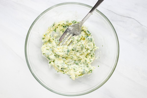 Garlic butter ingredients mixed in a bowl with a fork.