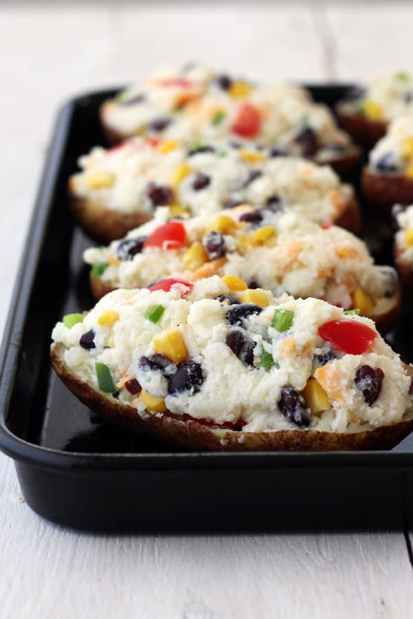 A dark baking sheet pan with unbaked stuffed potatoes.