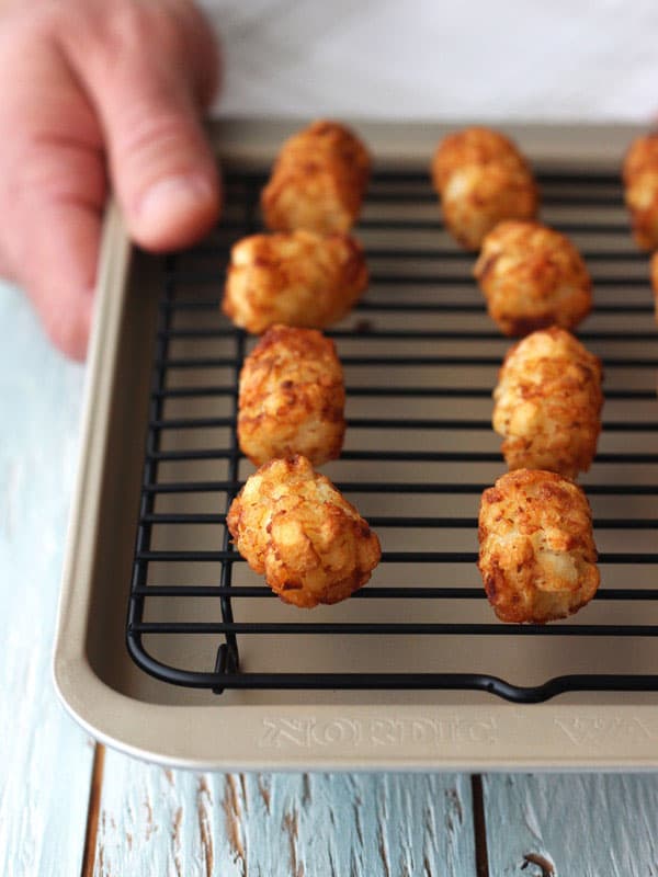 Hand holding small sheet pan of baked tater tots.