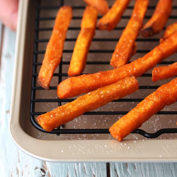 Close up of baked sweet potato fries on a small rack inside a sheet pan.