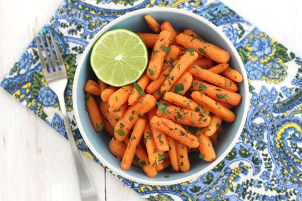 A blue bowl full of roasted carrots and half a lime wedge.