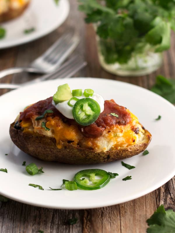 A twice baked potato on a white plate topped with Greek yogurt and sliced jalapenos.