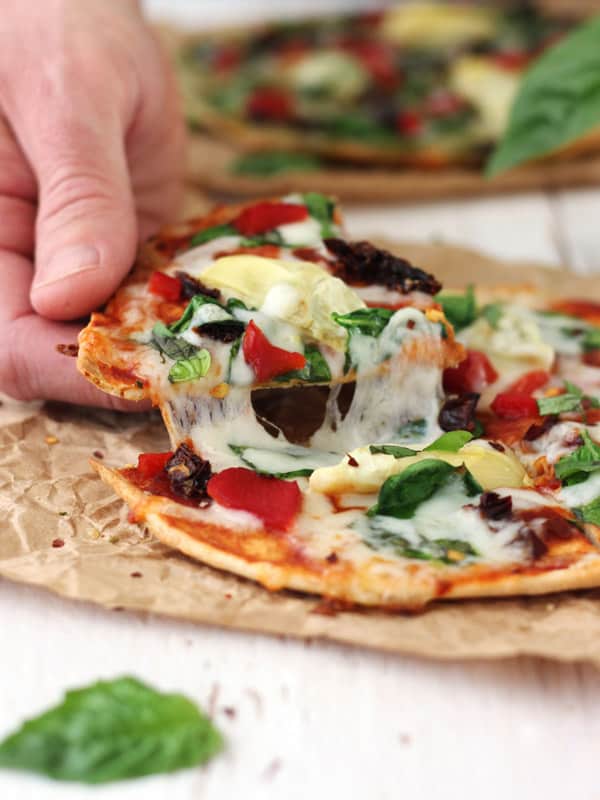A hand holding up a cheesy slice of tortilla pizza.