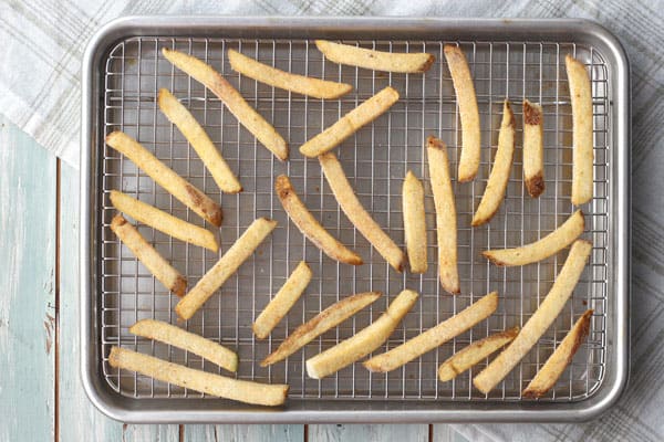 Frozen french fries on a rack inside a sheet pan.