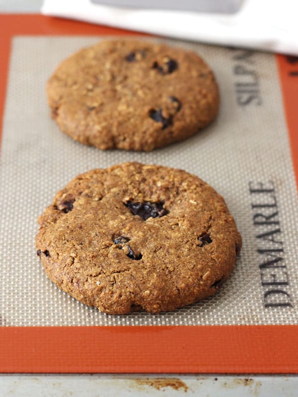 Two large oatmeal raisin cookies on a toaster oven silicone baking mat.