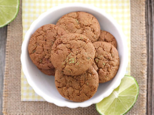 A small white bowl with cookies on a wooden table with lime wedges.