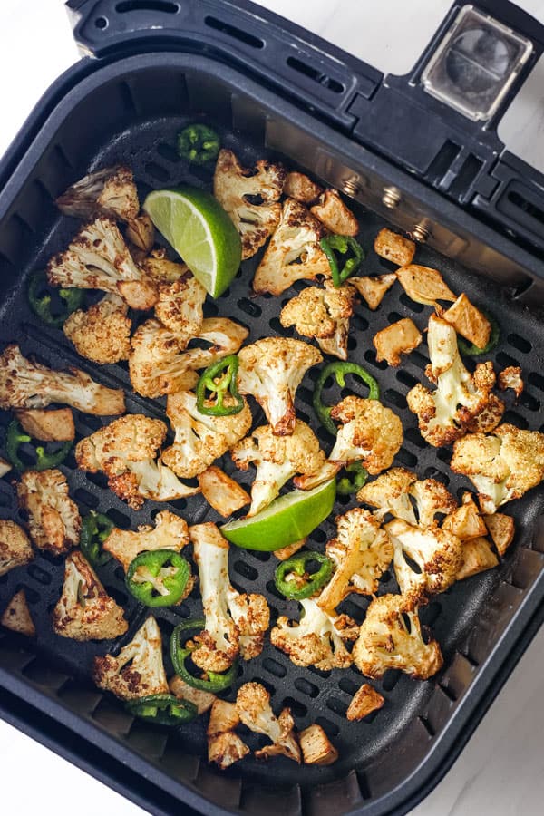 Air fryer basket with cauliflower and jalapeno slices.