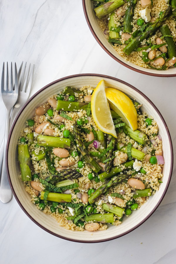 A tan bowl of salad on a white table with two forks.