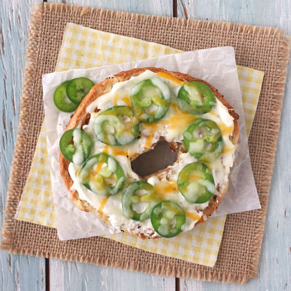 A toasted onion bagel topped with Greek yogurt cream cheese, jalapeno slices and shredded cheese.