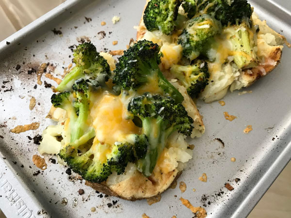 Two baked potato halves with roasted broccoli and melted cheese.