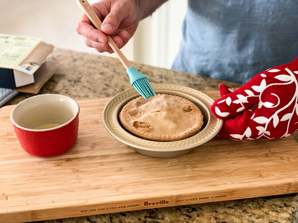 Hand brushing melted butter on a pot pie with a mini silicone brush.