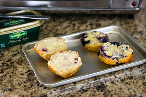 Buttered muffin halves on a toaster oven baking sheet.