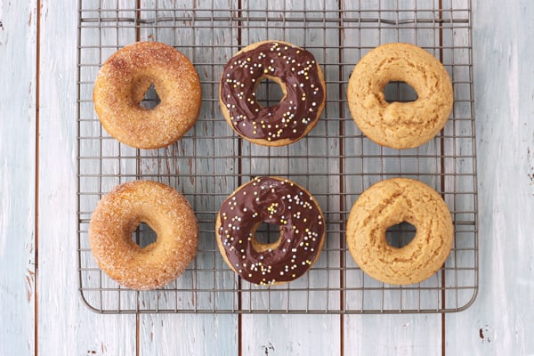 A cooling rack with donuts topped 3 ways: plain, cinnamon and sugar and with chocolate and sprinkles