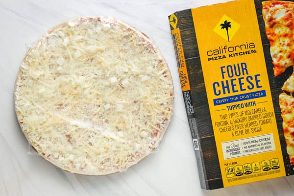 Frozen pizza in plastic next to pizza box.