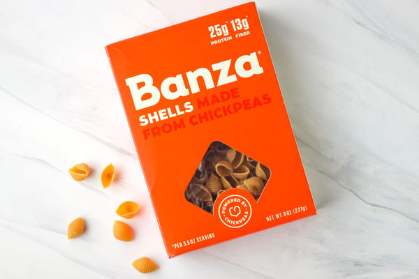 Orange box of Banza Chickpea Pasta Shells on a marble background.