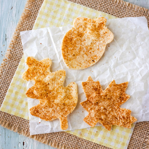 Leaf and acorn shaped tortilla chips on a piece of parchment paper.