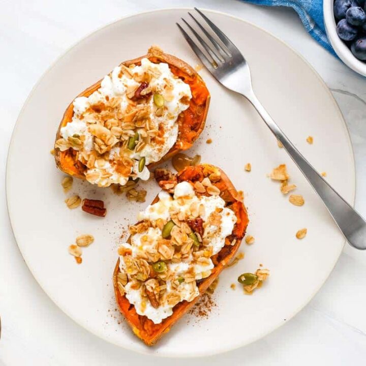 Topped sweet potatoes on a plate next to a jar of granola and bowl of blueberries.