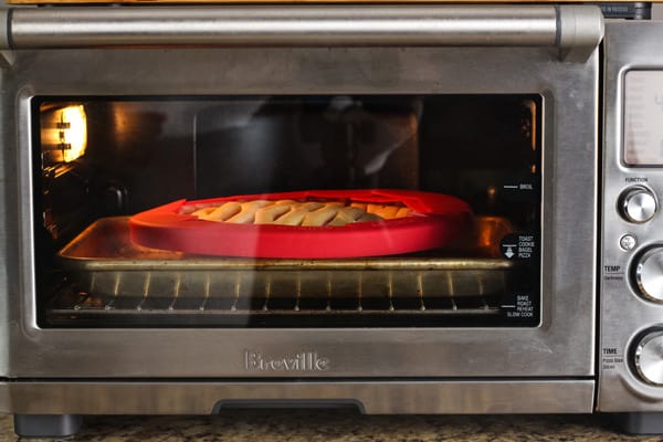 Pie with shield baking inside a toaster oven.