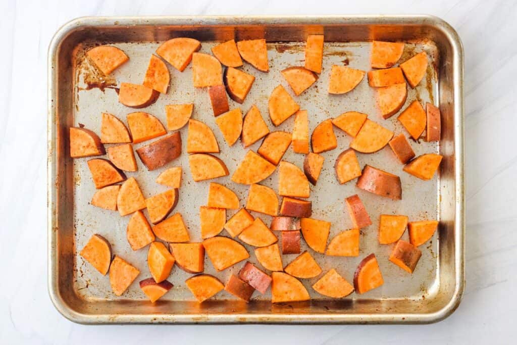 Seasoned sweet potato pieces on a sheet pan.