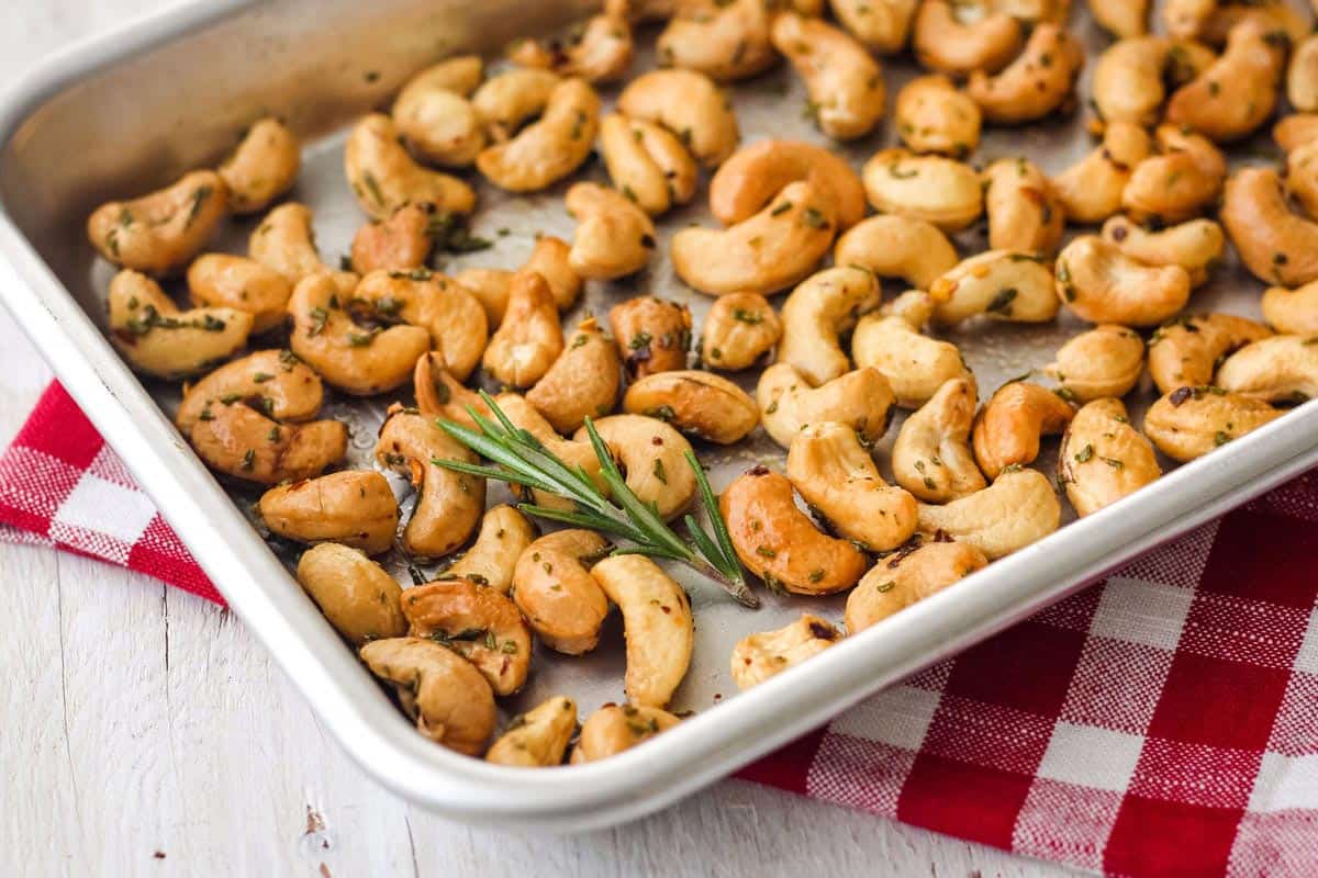 Closeup of small pan with roasted nuts and sprig of fresh rosemary.