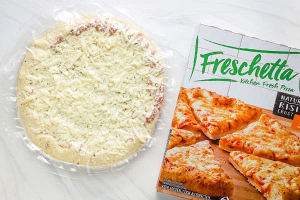Frozen pizza in plastic and pizza box on table.