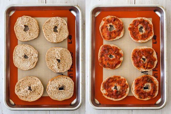 Plain bagels and bagels topped with pizza sauce on a silpat lined sheet pan.